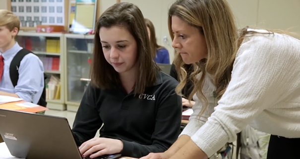 A teacher assists a student on a laptop computer